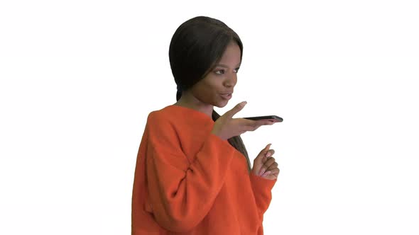 Pretty African American Woman in Bright Jumper Dictating Message Using Her Phone on White Background