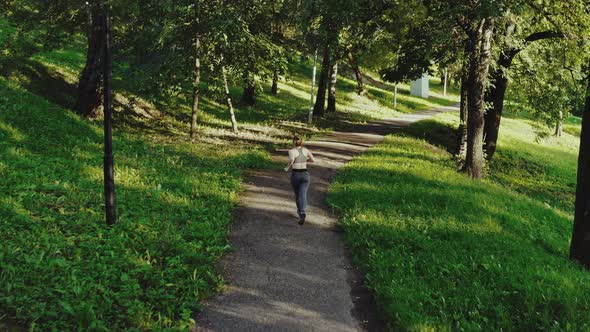 Young Attractive Girl Running in City Park. Woman Running in Wood Aerial Back View, Tracking Shot