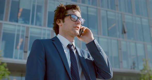 Medium Shot of Confident Businessman in Glasses Talking on Mobile Phone Outside