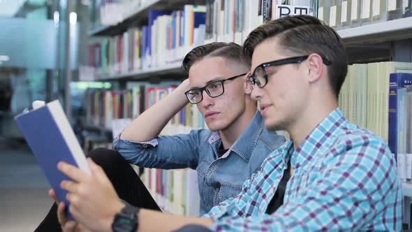 Students Reading Book At College Library Near Bookshelves