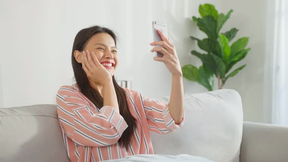 Asian attractive woman using mobile phone video call in living room.