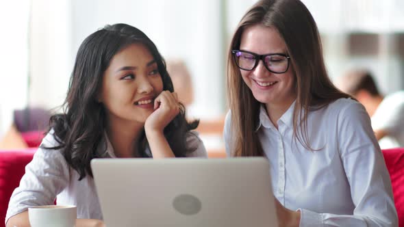 Two Young Smiling Businesswoman Friends Having Informal Team Meeting Using Laptop