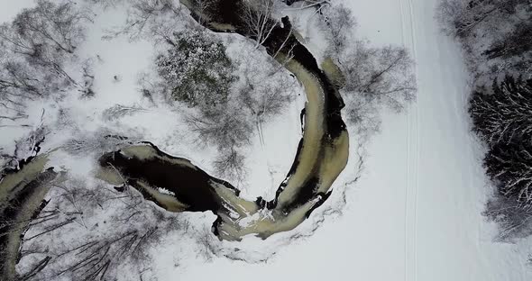Flying Over Dark Black River and Snow Covered Land