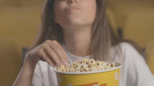 Close-up of Popcorn Box with Blurred Young Caucasian Woman Eating Snack at the Background. Positive