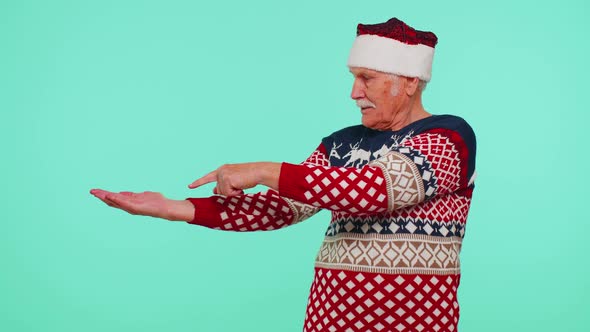 Grandfather in Santa Christmas Sweater Showing Thumbs Up and Pointing Empty Place Advertising Area