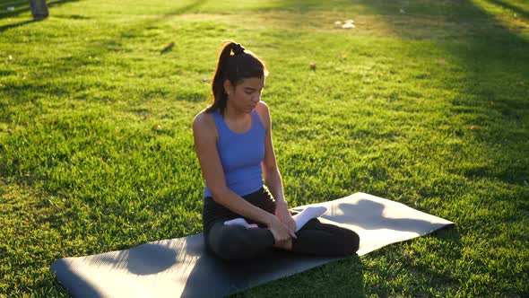 A fit young woman sitting in lotus position during meditation in the park at sunrise to improve her