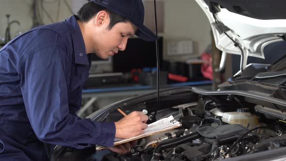 male mechanic checking and repair service a car with clipboard