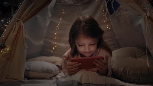 Adorable Small Girl Spending Time in Decorative Makeshift Hut with Lightings at Home in Evening