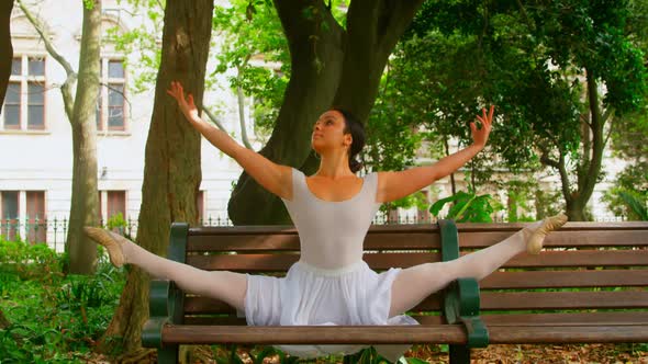 Young ballerina practicing dance on the bench in the park 4k