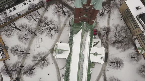 Rotating birds-eye view of vibrant green and red Saint Clare church in winter landscape,