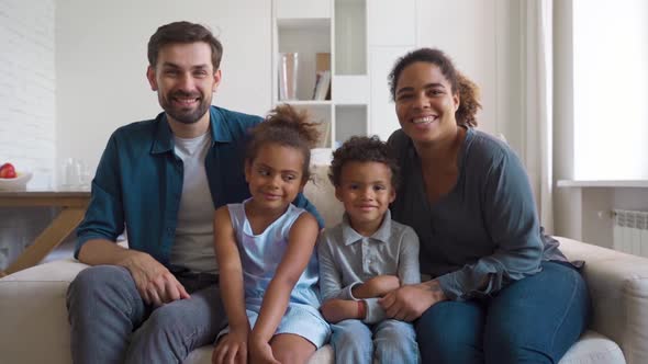 Happy Interracial Family with Children Sitting on Couch Looking at Camera