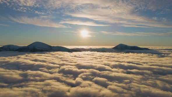 Aerial view of vibrant sunrise over white dense clouds with distant dark mountains on horizon.