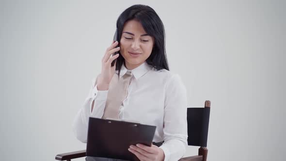 Portrait of a secretary in a blouse talking the mobile phone. Beautiful woman looking into the folde