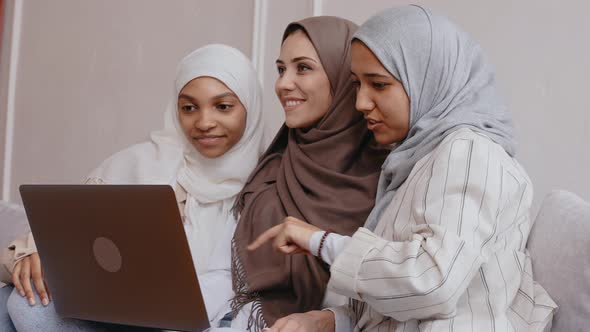 Three Muslim Girls Look at the Laptop Smile and Laugh in Bright Beige Studio