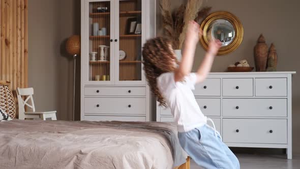 Preschooler Girl in Shirt and Denim Jeans Jumps Back on Bed