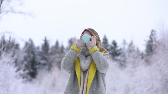 Beautiful woman in coat with cup of hot drink in a snow forest.