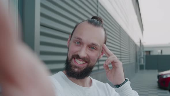 Shot of Young Bearded Guy Making Online Video Call Talking Looking at Camera Outdoors Holding Gadget