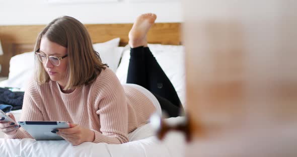 Woman using digital tablet and mobile phone in bedroom