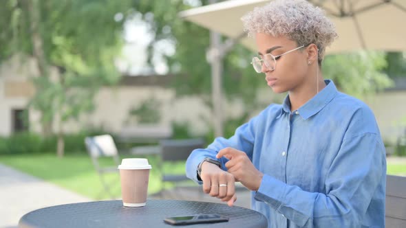 Young African Woman with Coffee Using Smart Watch in Outdoor Cafe