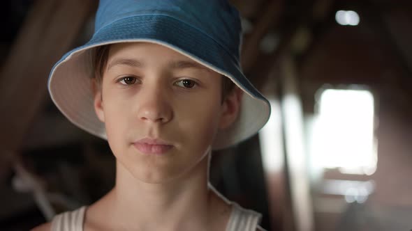 Portrait of a Happy Boy in a Blue Hat Looking at the Camera and Smiling Near the Window