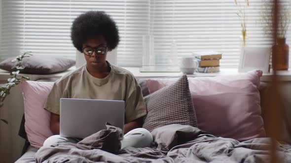 Thoughtful Black Woman Working on Laptop in Bedroom