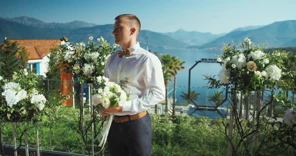 Groom on wedding ceremony with flowers waiting for bride against mountain and sea in Montenegro