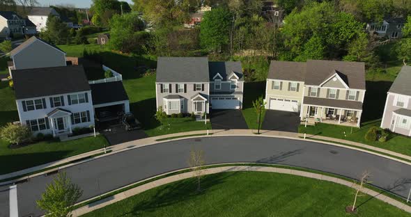 Curve of street and new houses. Neighborhood gathering and people outside garage. Aerial view.