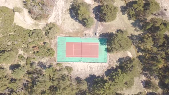 An old tennis court in red and green with many trees around. Drone shot ascending