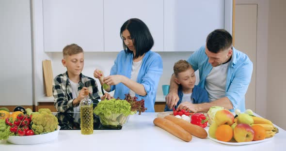 Two Brothers Helping to Cook Vegetable Salad with their Good-Looking Smiling Young Parents