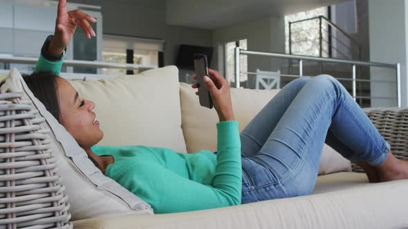 Mixed race woman lying on couch having video chat on smartphone blowing kisses