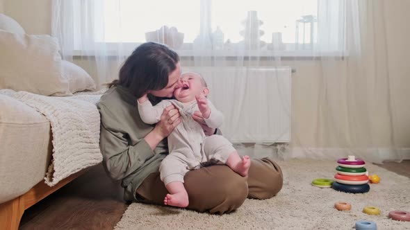 The mother kisses the happy laughing baby and hugs him. Mom amuses a smiling, happy child