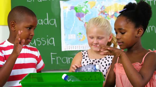 School kids putting waste bottle on recycle logo box in classroom