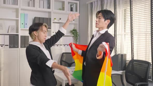 Asian businessman gay dancing in office workplace and hold LGBTQ flag. Homosexual-LGBTQ concept