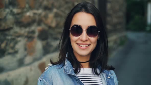 Portrait of Girl with Dark Hair in Sunglasses Standing Outside