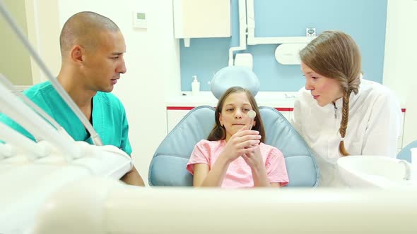 Dental assistant and dentist showing mouth mirror to little girl before check up