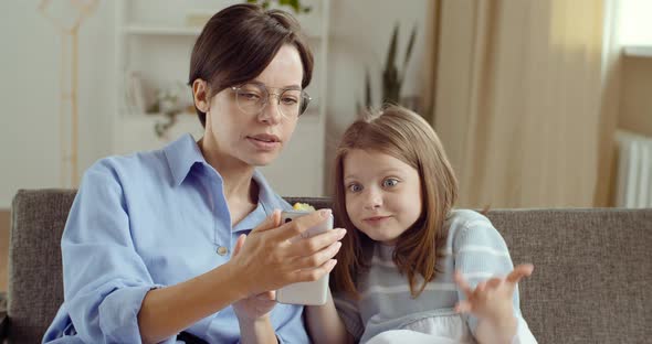 Young Mother with Glasses Sister Nanny Sitting with Her Daughter Girl Looking at Phone Together