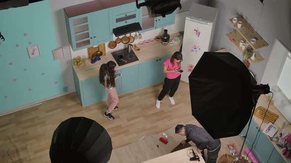 View From Above of Young Girls Bloggers Using Phone to Watch Videos on Social Networks in Kitchen