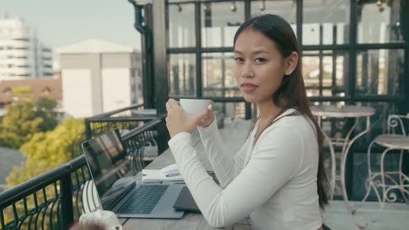 A Young Asian Girl Works at Her Laptop in a Rooftop Cafe in the City