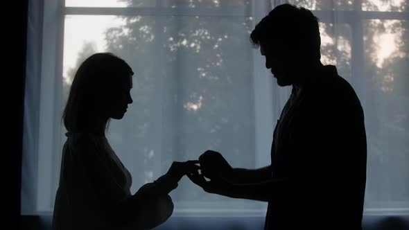 Silhouettes of Man and Woman Groom Putting Engagement Ring to the Bride in the Evening at Home