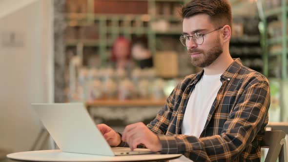 Young Man with Laptop Smiling at Camera in Cafe