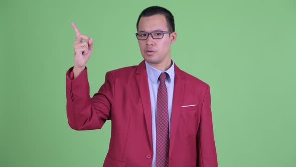 Happy Asian Businessman with Eyeglasses Talking While Pointing Up