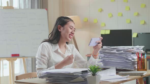 Asian Woman Being Upset Losing Game On Smartphone After Working With Documents At The Office