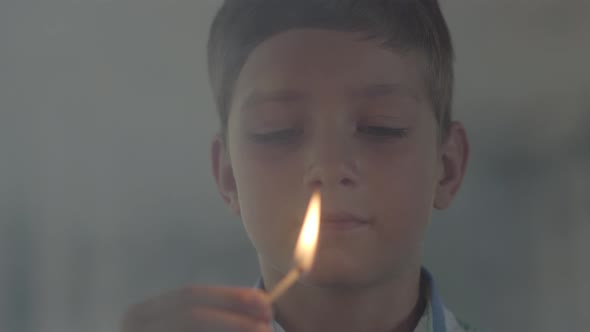 Close-up Portrait of Little Boy Playing with the Matches in the Dark Smoky Room