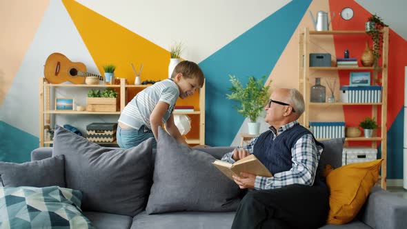 Elderly Man Reading Book at Home When Grandson Coming Doing High-five Laughing