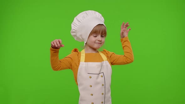 Child Girl Kid Dressed in Apron and Hat Like Chef Cook Baker Raising Hands Showing Tasty Gesture