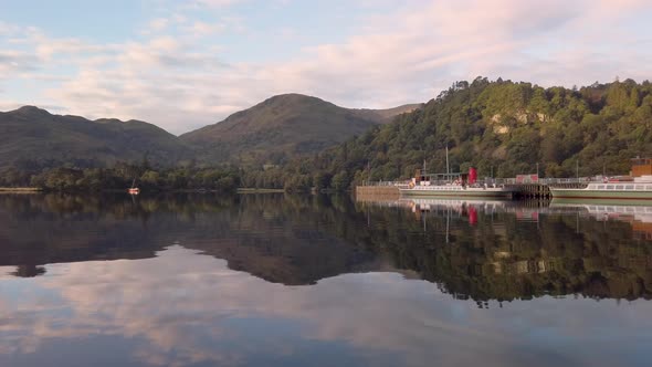 Reflections on calm Ullswater Lake of boats, hills and woodland