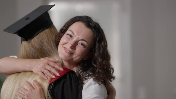 Glad Caucasian Woman Hugging Female Graduate Indoors Looking at Camera Smiling