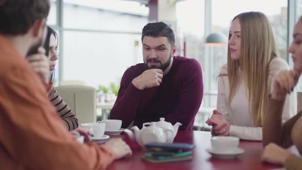 Group of Digital Addicted Caucasian Friends Chatting in Cafe and Looking at Blurred Devices Lying on