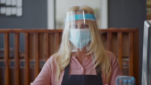 Senior Waitress in Medical Protective Mask and Plastic Face Shield Serving Restaurant