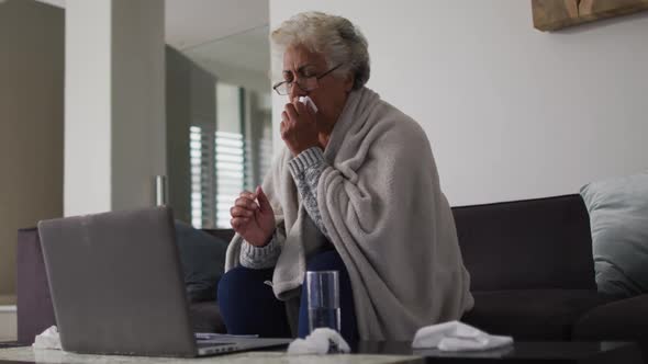 Sick african american senior woman coughing while having a video call on laptop at home